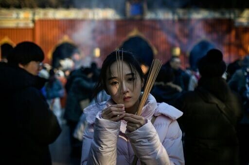 A woman burns incense sticks and offers prayers at Yonghe Temple, also known as Lama Temple, on the first day of the new year in Beijing on January 1, 2026