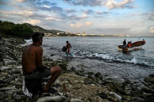 Fishermen work at a local beach, with the El Palito refinery visible in the distance