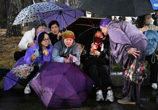 BTS fans react as they watch a live concert by K-pop boy band BTS on their mobile phones outside a stadium where the group is performing in Goyang on April 9, 2026.