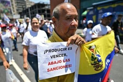 A protester in Caracas holds a sign reading "to produce is to win; down with sanctions"