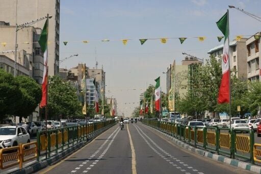 Vehicles drive along a street adorned with Iranian flags at Revolution Square in Tehran