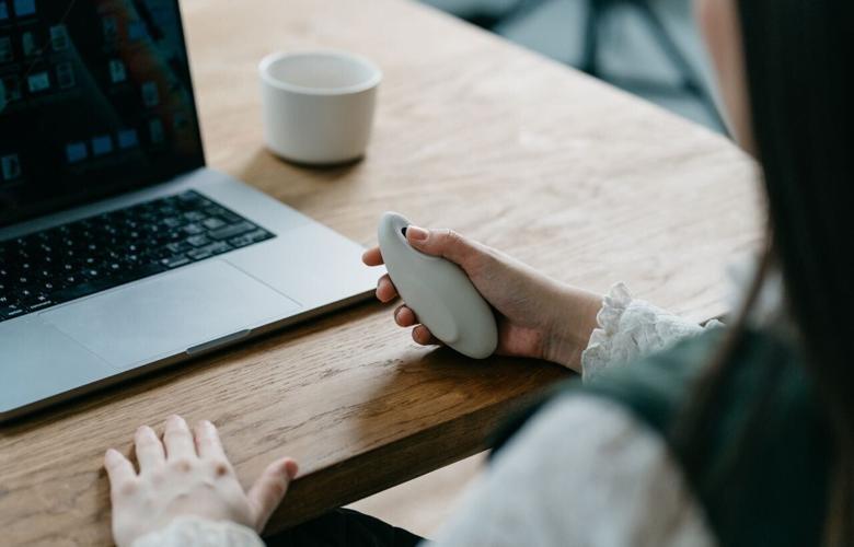 Woman using laptop while holding Moonbird breathing coach.