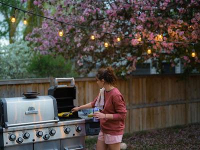 Cheerful woman grilling on the backyard of her house in springtime