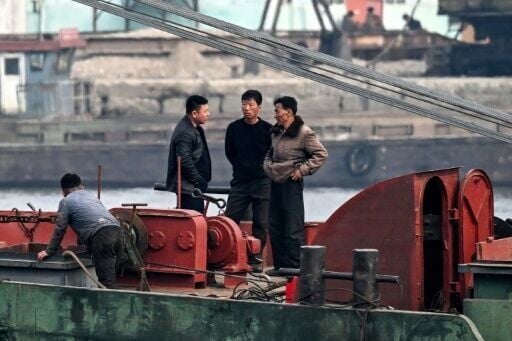 North Korean men converse aboard a dredge operating on the Yalu River, with the North Korean city of Sinuiju visible in the background, opposite the border city of Dandong in China’s northeastern Liaoning province on March 24, 2026