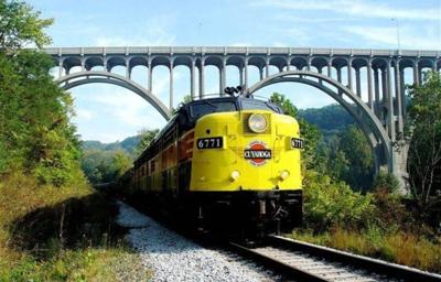 Yellow train passing beneath arched bridge