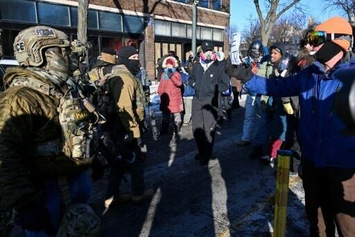 Federal agents (L) look on as demonstrators gather near the site a fatal shooting in Minneapolis