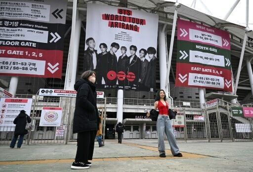 A woman poses in front of a large banner featuring K-pop boy band BTS at a stadium where the group will perform in Goyang on April 9, 2026.
