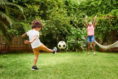 Shot of a little boy playing football with his grandmother in backyard