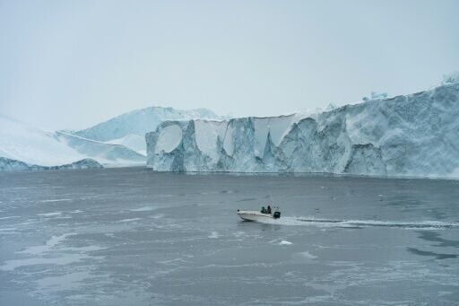 A small motorboat passes in front of icebergs not far from Ilulissat as the ferry passes