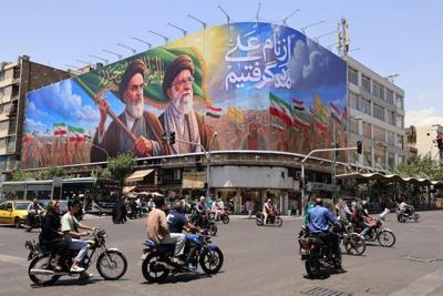 People ride motorcycles past a large billboard in central Tehran on June 8, 2026.