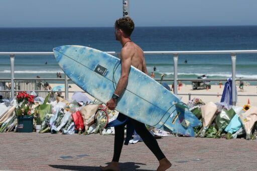 A surfer walks past floral tributes left at the promenade of Bondi Beach in Sydney on December 18, 2025, to honour victims of the shooting that took place there on December 14.