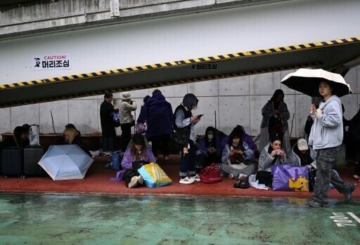 BTS fans take shelter from the rain as they arrive at a stadium where K-pop boy band BTS will perform in Goyang on April 9, 2026.