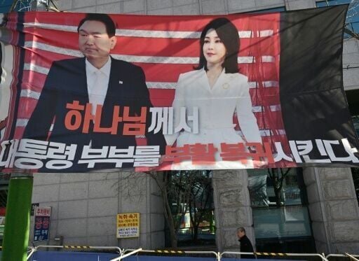 A man walks past a banner showing a picture of South Korea's former impeached president Yoon Suk Yeol and his wife Kim Keon Hee in Seoul.