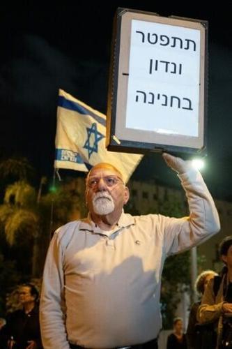 A demonstrator holds a sign reading in Hebrew: 'Resign and we will discuss a pardon'