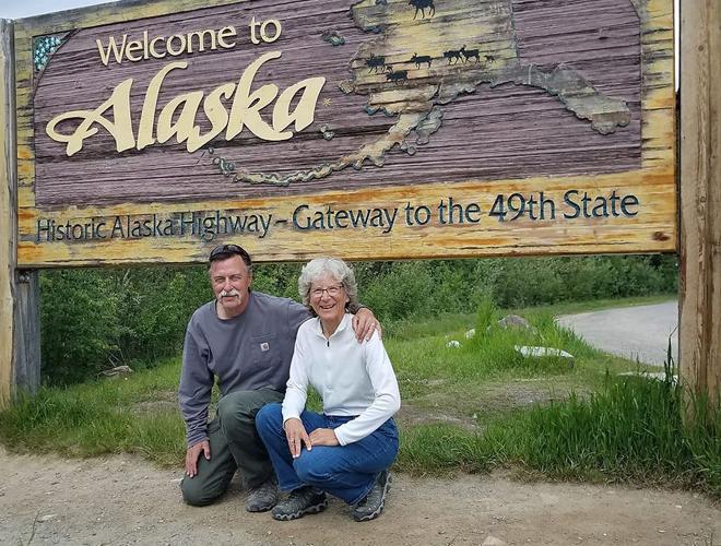 Rochelle Renken and Michael Huffman in front of a "Welcome to Alaska" sign