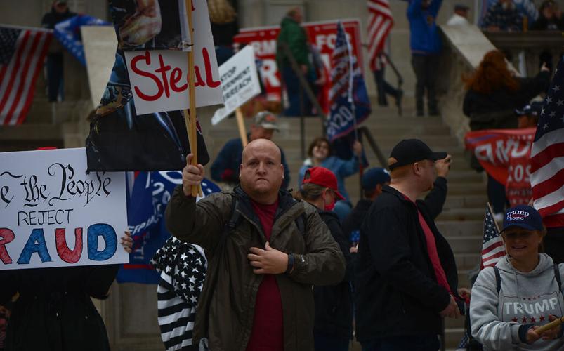 A Trump supporter holds up a flag and a sign in front of a crowd in front of the Missouri State Capitol