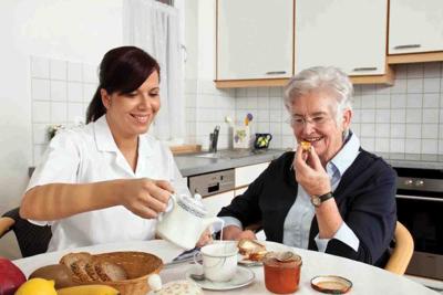 nurse helps elderly woman at breakfast