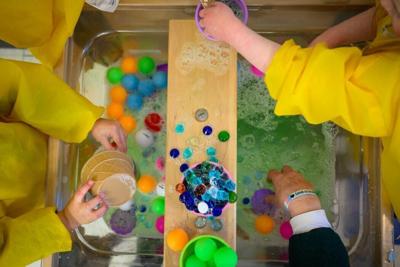 Students play with toys in a basin of soapy water at a child care center in New Britain, Conn., in March 2025.
