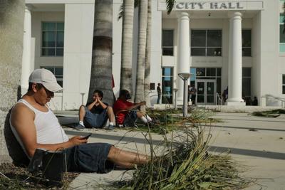 Residents without power at home charge their mobile phones using electrical outlets at the base of palm trees at City Hall in Homestead, Fla., after Hurricane Irma in September 2017.
              Chip Somodevilla/Getty Images