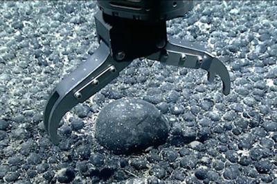A metal claw reaches for an iron and manganese nodule on the seabed for testing.