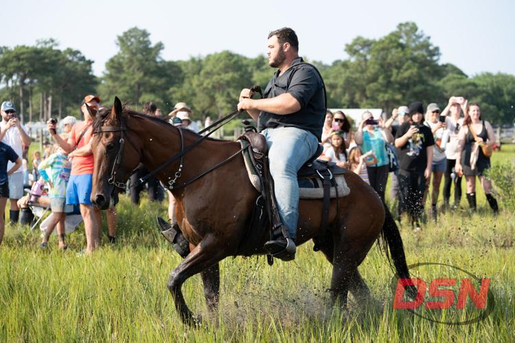 Saltwater Cowboy on horseback splashing through the marsh in front of the crowd.jpg