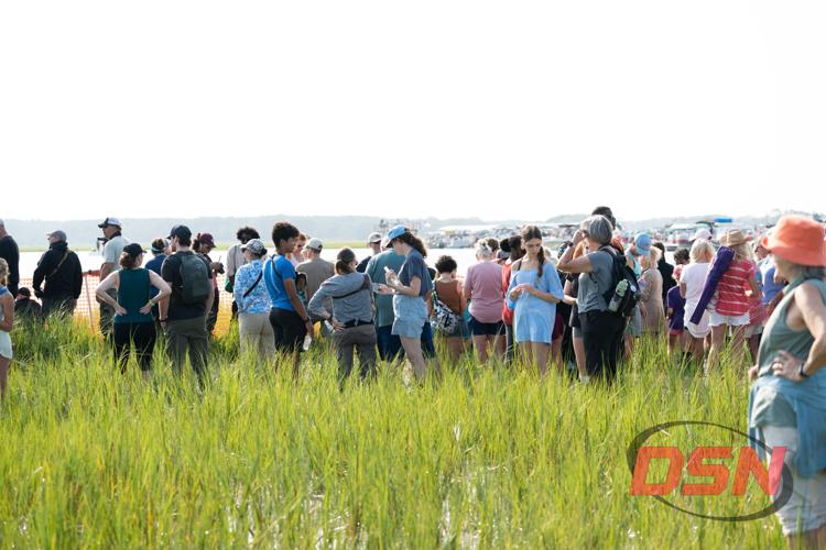 Large crowd gathered in the marsh grass with boats in the channel.jpg
