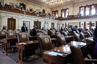 Texas House chamber with several empty desks in the foreground, and people in the background.