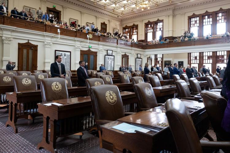 Texas House chamber with several empty desks in the foreground, and people in the background.