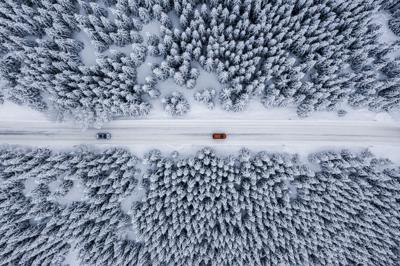 Fir tree forest and a road covered with snow seen from a drone perspective