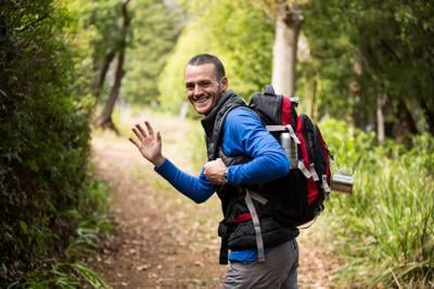 Male hiker waving hand while walking in forest Photo Credit: Wavebreakmedia (iStock).