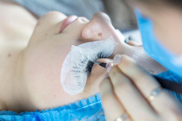 Woman gets false eyelashes applied by professional, to maintain groomed facial appearance