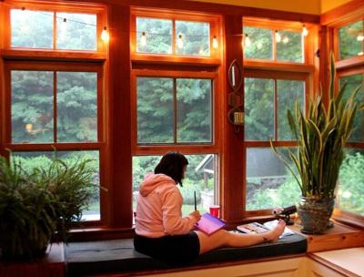 Woman sits in window peacefully working on diamond painting as form of mindfulness