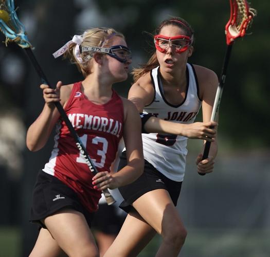 Two women lacrosse players on opposite teams run beside each other