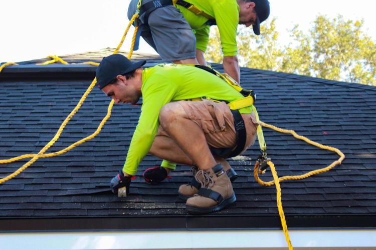 Men work on new roofing shingles at persons home