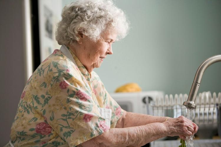 Senior woman washes vegetables at the sink of her senior care facility