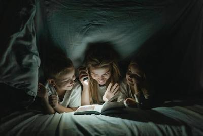 Children read book under covers using small flashlight