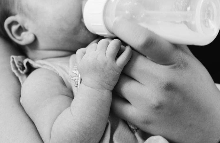 Baby is fed milk in a bottle after showing hunger cues