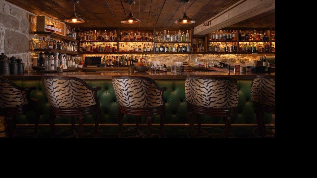 The Speakeasy bar at San Ysidro Ranch in Montecito with backlit bottles, warm lighting, stone walls, and patterned bar chairs.