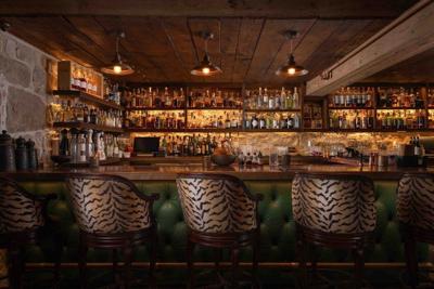 The Speakeasy bar at San Ysidro Ranch in Montecito with backlit bottles, warm lighting, stone walls, and patterned bar chairs.