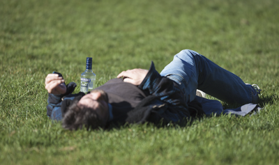 Man sprawls on grass next to empty liquor bottle