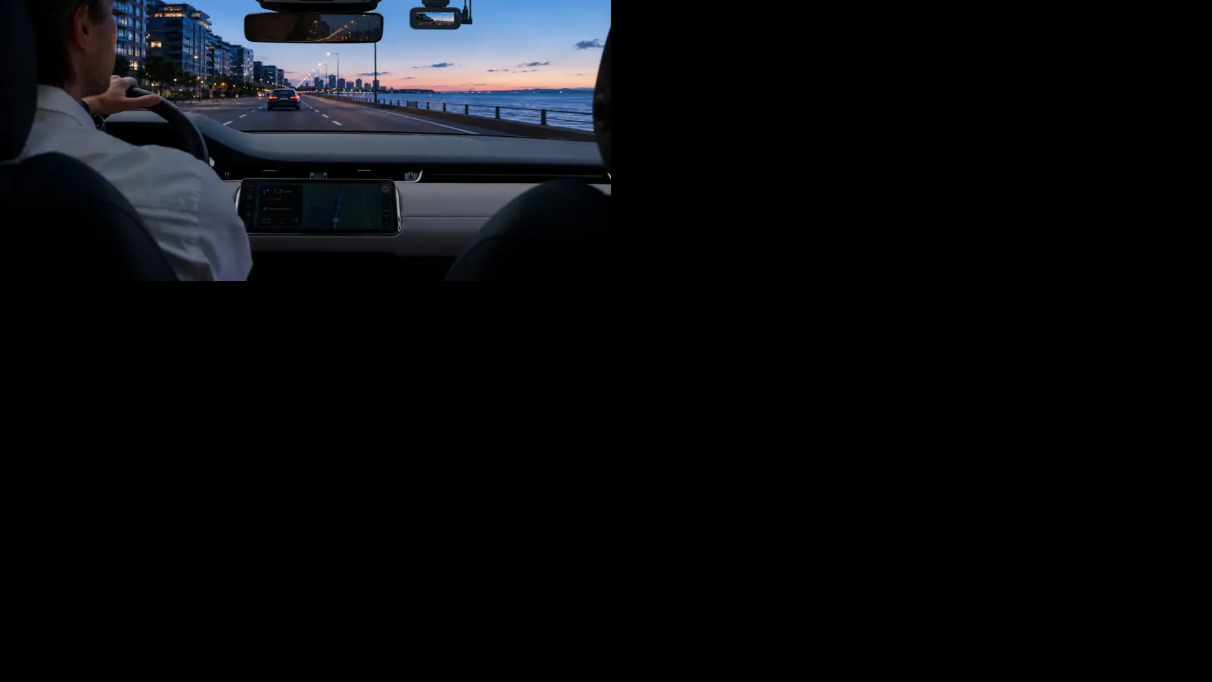 70mai A900 dash camera mounted inside a vehicle overlooking a waterfront road at sunset.