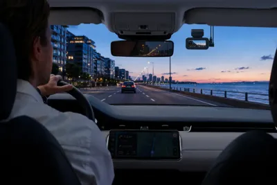 70mai A900 dash camera mounted inside a vehicle overlooking a waterfront road at sunset.