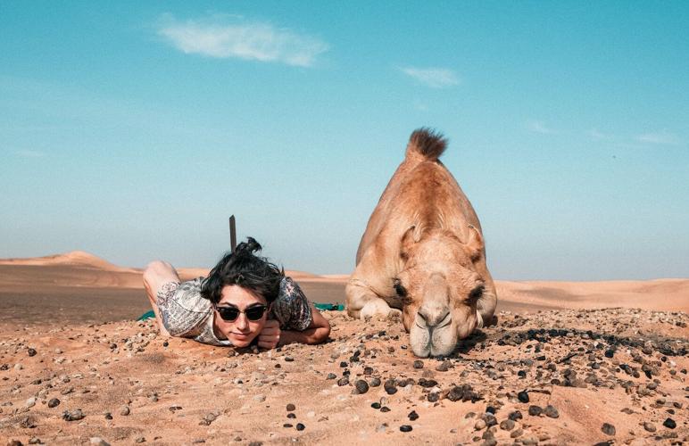 Man lies next to camel on budget-friendly vacation