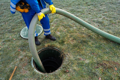 Man feeds tube into hole in ground as part of septic cleaning service