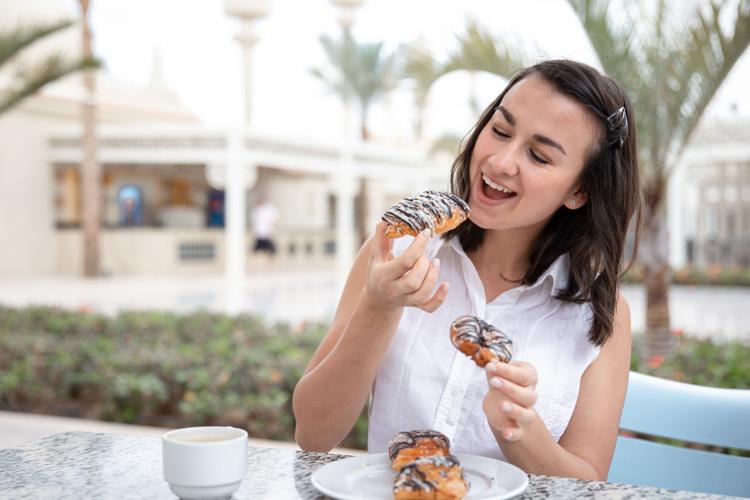 Young happy woman enjoying coffee and pastries on the outdoor summer terrace.