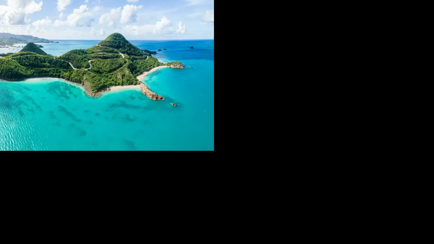 Aerial view of Pearns Point in Antigua surrounded by turquoise Caribbean water and green hills.