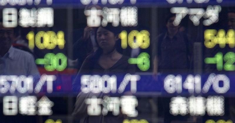Woman is reflected in a stock index board outside a brokerage in Tokyo