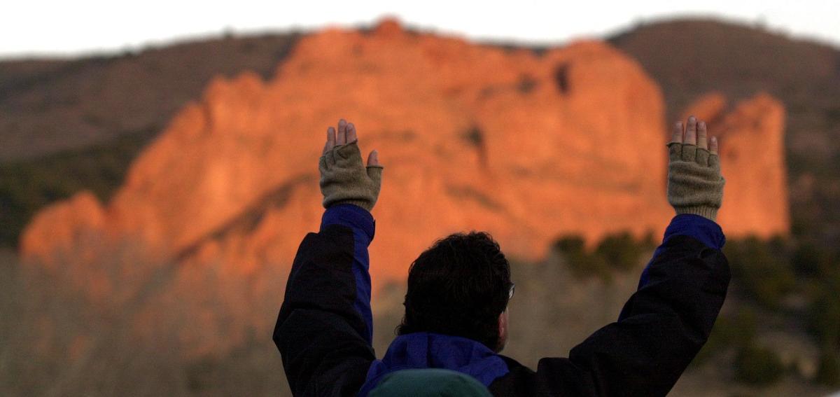 Sunday, April 15, 2001-photo by Jerilee Bennett-The annual Easter Sunrise Celebration was held at dawn in the meadow near Rockledge Ranch. Lee O' Brien raises his hands in praise as the Kissing Camels rocks are lit up by the first rays of light. The event was sponsored by Pierce Chapel.