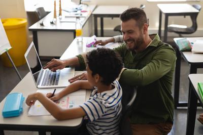 Young school teacher helping boy with study on laptop in classroom