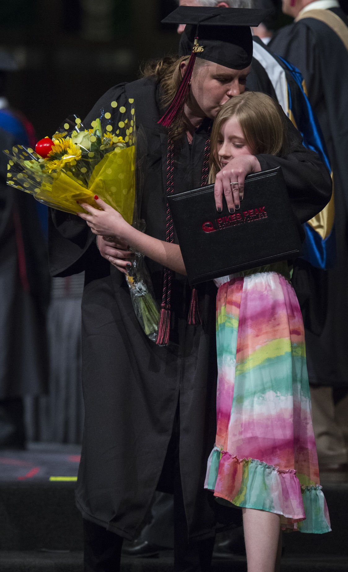 Jocelyn Andersen, 9, greets her mother, Pam Andersen, at the side of the stage with flowers and a hug after she received her diploma during the commencement ceremony for The Pikes Peak Community College class of 2016 May, 14, 2016, at New Life Church in Colorado Springs. See Gazette.com for photo galleries from 60 area graduations including Pikes Peak Community College. (The Gazette, Christian Murdock)